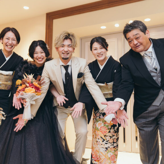 黒のドレスの花嫁とベージュのタキシードの新郎が、留袖やモーニング姿のご家族とポーズをとる集合写真