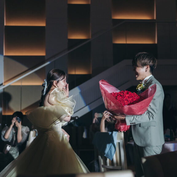 暗転した会場でスポットライトを浴び、新郎が花嫁に赤いバラの花束を贈るサプライズの瞬間