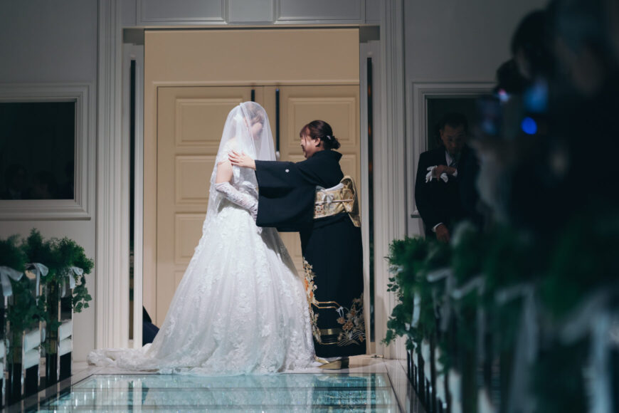 チャペルの扉の前で新婦にベールダウンをするお母さま