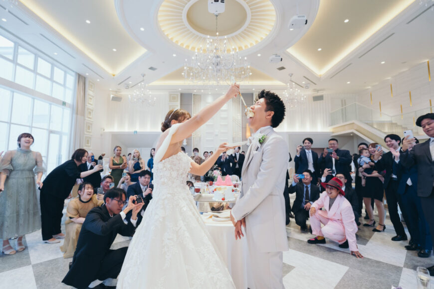 ゲストに囲まれて大きなスプーンでファーストバイトをする新郎新婦